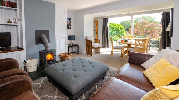 Ein gemütliches Wohnzimmer mit Kamin, einer Couch, einem Couchtisch und einem Essbereich mit Gartenblick.