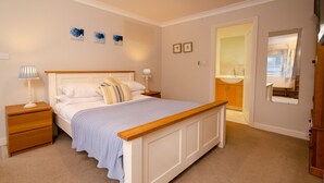 A bedroom with a bed, nightstands, a wooden headboard, a carpeted floor, and a bathroom visible through an open door.