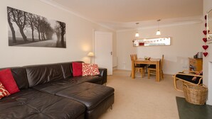 A living room with a leather sofa, a dining table with chairs, a mirror with heart decorations, and a framed picture on the wall.