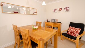 A dining area with a wooden table, four chairs, a bowl, a mirror, a clock, a radio, and a decorative wall piece.