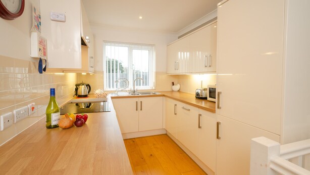 A modern kitchen with white cabinets, a wooden countertop, and a window providing natural light.