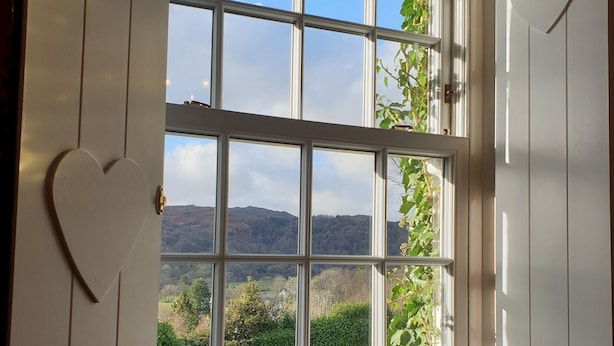 Una habitación con un amplio ventanal que da a un paisaje pintoresco, una decoración con forma de corazón en la pared y un banco estampado.