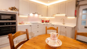 Una cocina moderna con armarios blancos, una mesa de comedor de madera y un hervidor rojo.