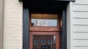 A wooden door with a glass panel, a plaque on the wall, and a view of the street through the glass.