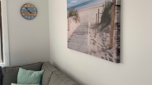 Un soggiorno con un divano grigio, un orologio appeso al muro e un quadro raffigurante una spiaggia.