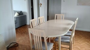 Zona pranzo con tavolo rotondo e sei sedie, un divano grigio sullo sfondo e un pavimento in legno a spina di pesce.