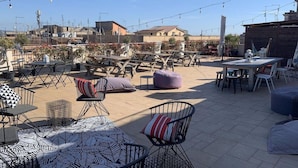 Un patio exterior con mesas y sillas, luces colgantes y vistas del barrio circundante.