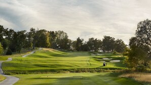 Un parcours de golf avec un chemin sinueux, des bunkers de sable et quelques personnes.