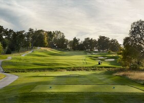 Un campo de golf con un camino sinuoso, búnkeres de arena y algunas personas.
