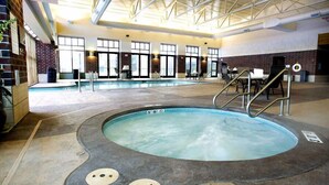 Une piscine intérieure avec un jacuzzi, entourée de fenêtres et d’un mur en briques.