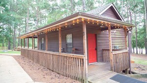 A wooden cabin with a porch, a red door, and string lights. - studio rm w/ full kitchen, 1 bth , private deck, & WiFi @ Kick Back Ranch. (Ramer)