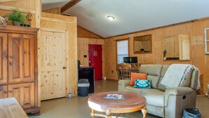 A cozy room with wooden walls, a sofa, a coffee table, and a television. - studio rm w/ full kitchen, 1 bth , private deck, & WiFi @ Kick Back Ranch. (Ramer)