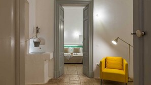 A narrow hallway leading to a bedroom with a bed, a small table with a lamp, and a yellow chair. - Masseria Pugliese Deluxe (Ostuni)