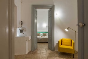 Un estrecho pasillo que conduce a un dormitorio con una cama, una mesita con una lámpara y una silla amarilla.