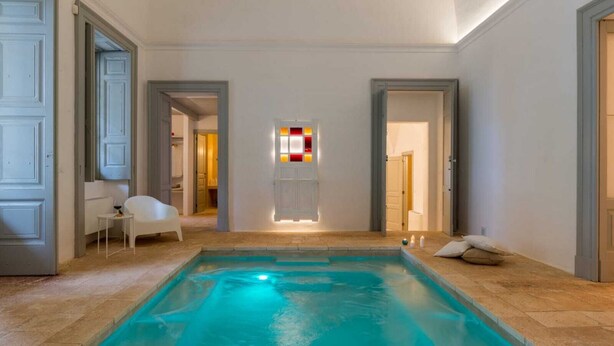 A swimming pool with a tiled floor, a white chair, and a door leading to another room. - Masseria Pugliese Deluxe (Ostuni)