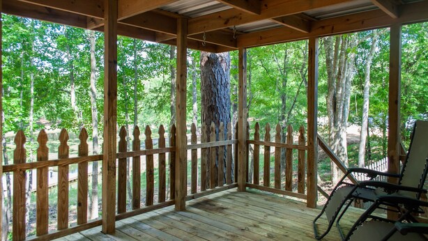 Une terrasse en bois avec une rambarde en métal, entourée d’arbres.