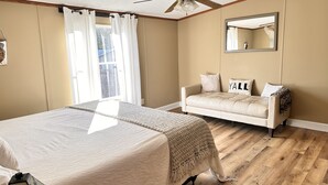 Une chambre à coucher comprenant un lit, un canapé, un ventilateur de plafond, une fenêtre avec des rideaux et un miroir au mur.