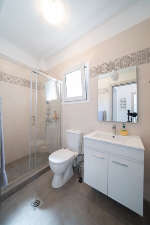 Ein Badezimmer mit Duschkabine, einer weißen Toilette, einem Waschbecken mit Spiegel darüber und einem gefliesten Boden.