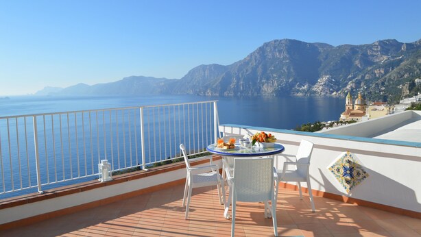 A balcony with a table and chairs overlooking a sea view with mountains in the background. - La Gemma di Praiano (Praiano)