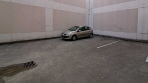 En parkeringsplads med en bil parkeret i et hjørne, betonvægge og et afløb i jorden.