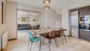 Et moderne køkken med indbygget ovn og køleskab, et spiseområde med et træbord og stole, og en stue med sofa og kunstværker.