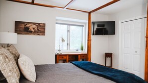 A bedroom with a bed, a desk, a window, and a TV mounted on the wall.