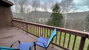 A wooden deck with two blue chairs and a railing overlooking a grassy area with trees and hills.