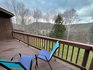 A wooden deck with two blue chairs and a railing overlooking a grassy area with trees and hills.