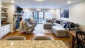 A modern living room with a fireplace, a dining area, and a kitchen.