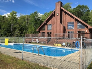 A wooden cabin with a swimming pool surrounded by a chain-link fence.