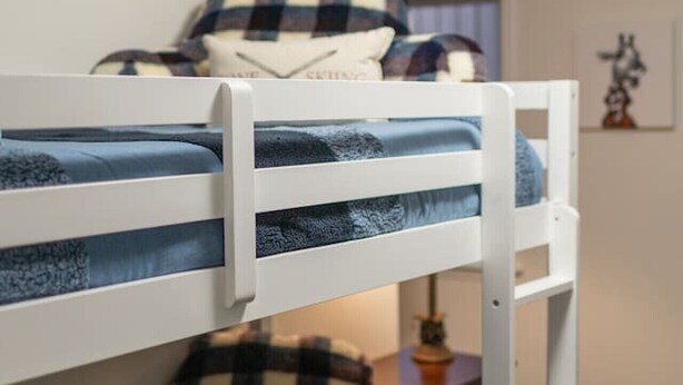 A bunk bed with a checkered blanket and pillows, a small table with a lamp, and a framed picture on the wall.