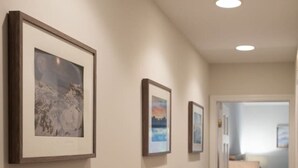 A hallway with three framed pictures on the wall, leading to a bedroom with a bed and a nightstand.