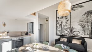 A modern kitchen with a dining area, a sofa, and a large tropical-themed artwork.