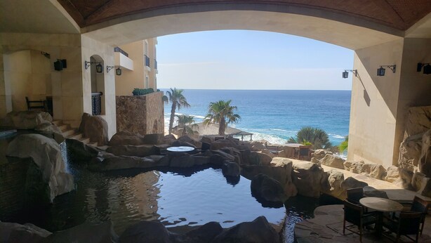 A pool area with a view of the ocean, surrounded by stone walls and furnished seating. - Private Oceanfront Luxury (Cabo San Lucas)