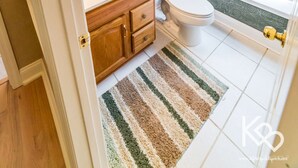 Une salle de bain avec un lavabo blanc, un meuble-lavabo en bois, des toilettes et une fenêtre avec des stores.