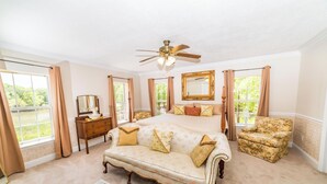 Une chambre à coucher avec un grand lit, une table de chevet, une commode, une chaise et un ventilateur de plafond.