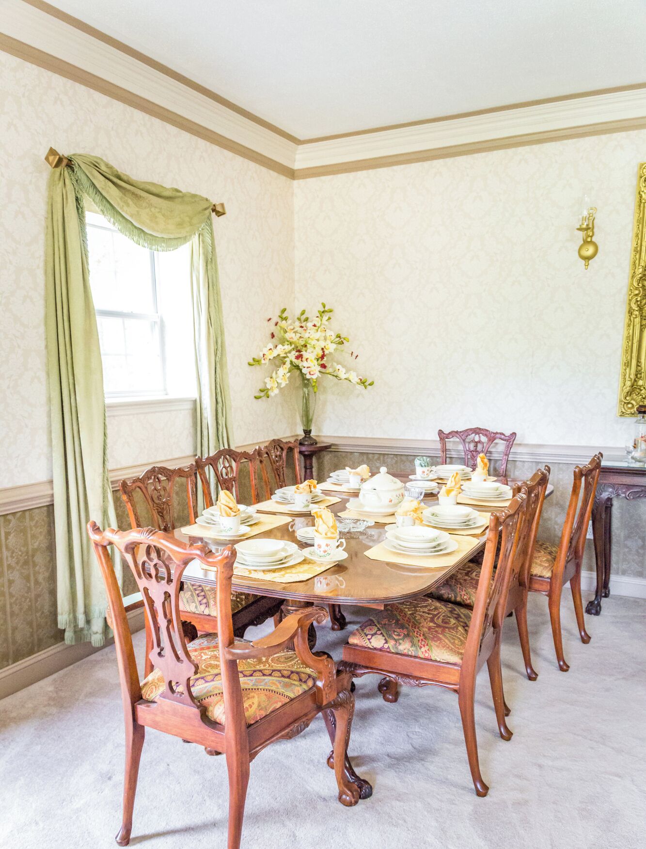 Une salle à manger élégante, avec une grande table en bois dressée pour un repas, entourée de chaises richement décorées.