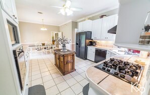 A modern kitchen with white cabinets, a built-in stove, and a dining area with a wooden table and chairs. - The Ada Estate Home at Kick Back Ranch & Event Center, 8br 4.5bth, Accom. 20 (Ramer)