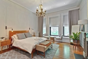 A bedroom with a large bed, bedside tables, a bench, a chandelier, a chair, a plant, and a fireplace. - Historic luxury townhouse on Chicago's Gold Coast (Chicago)