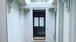 Un pasillo estrecho con paredes de ladrillo blanco, piso de madera y una puerta negra al final.