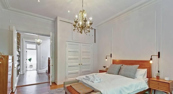 A bedroom with a wooden headboard, a large bed, bedside tables, a chandelier, and a wardrobe.