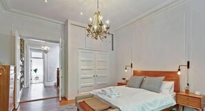 Une chambre Ă coucher avec une tĂȘte de lit en bois, un grand lit, des tables de chevet, un lustre et une armoire.