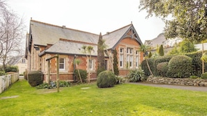 A two-story house with a brick facade, a sloped roof, and a well-maintained garden with hedges and a lawn. - Charming Schoolhouse Apartment by Fowey Harbour (Cornwall)