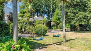 A garden with a wooden swing set and a stone pathway. - Charming Schoolhouse Apartment by Fowey Harbour (Cornwall)