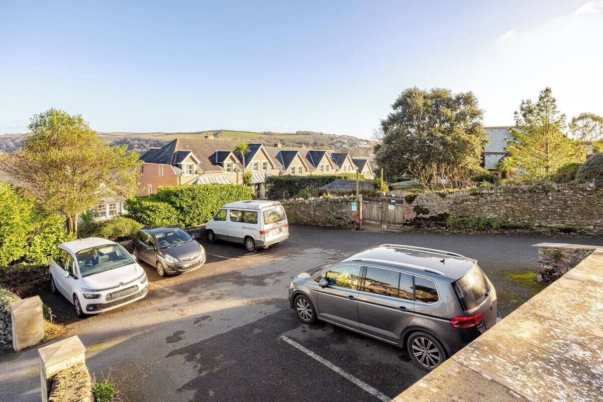 A parking area with several cars and a van, surrounded by stone walls and greenery.