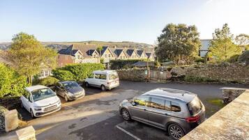 A parking area with several cars and a van, surrounded by stone walls and greenery.