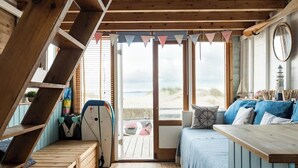 Una habitación acogedora con techo de madera, cama con ropa de cama azul, una mesa de madera y una tabla de surf apoyada en la pared.