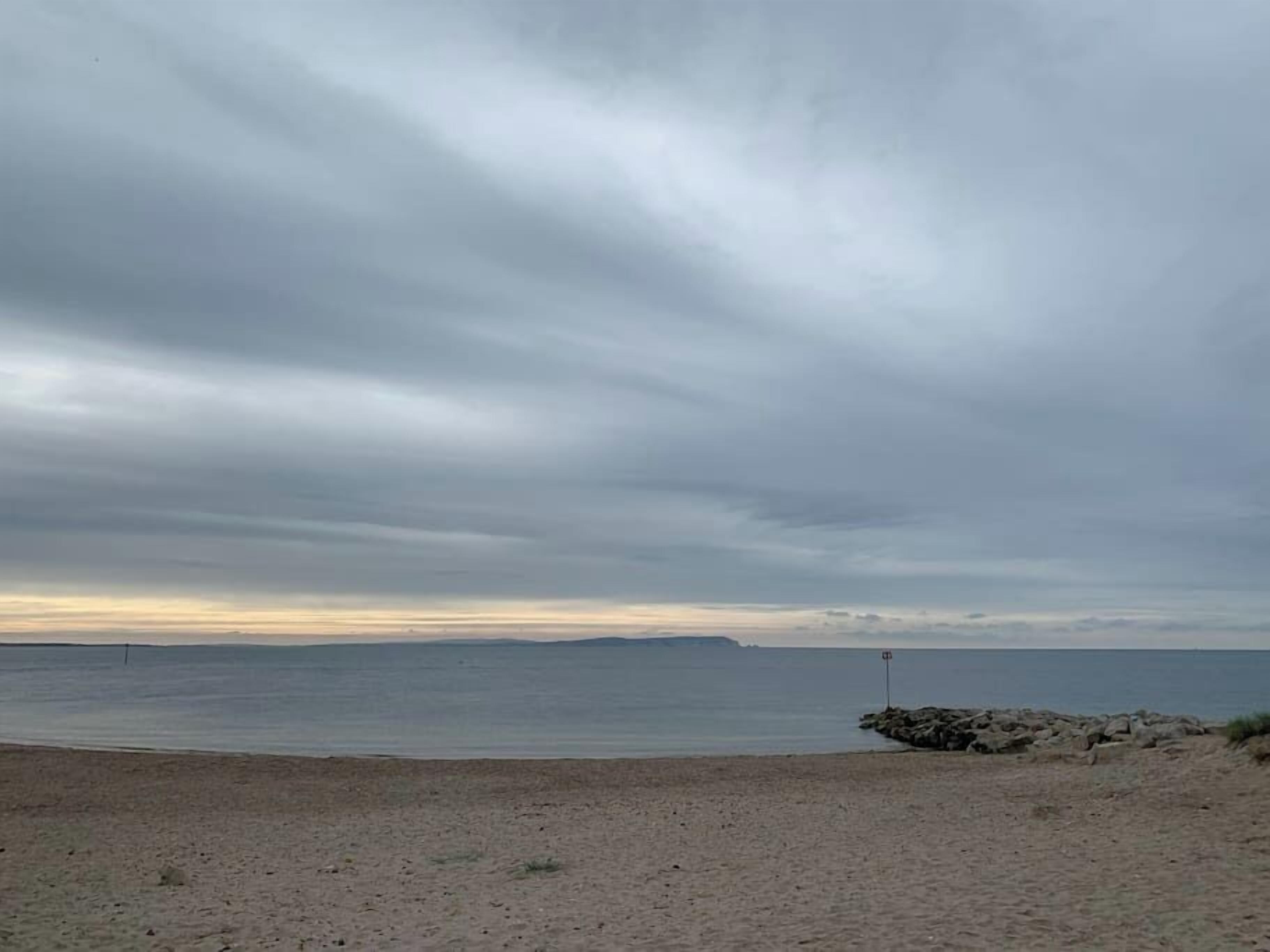 A beach with a rocky outcrop and a calm sea under a cloudy sky.