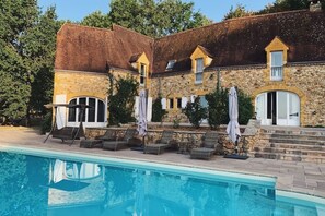 A stone building with a swimming pool, outdoor seating, and a staircase leading to a door.