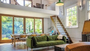 Een ruime woonkamer met een eettafel, een groene bank en een trap naar een hoger gelegen verdieping.